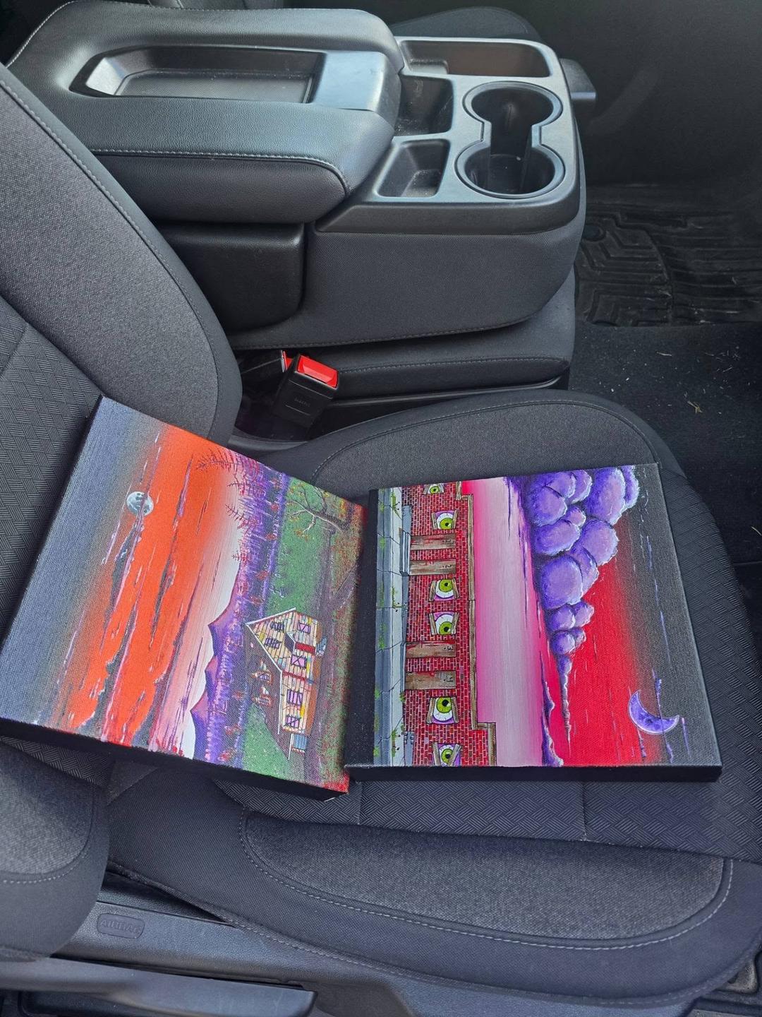 The two gallery paintings laid out on the passenger seat of a car on delivery day